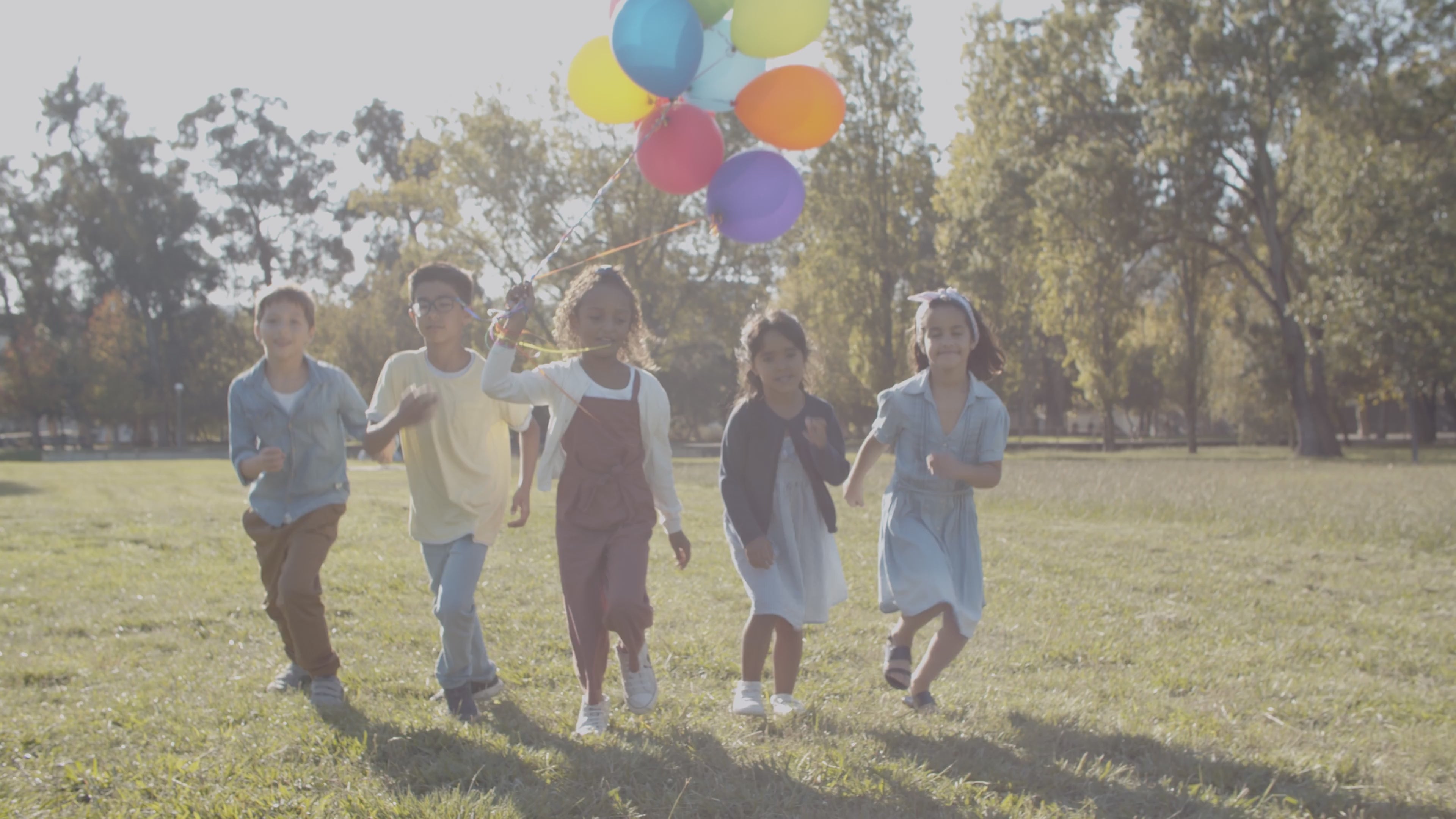 niñas y niños en un parque corriendo con globos