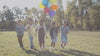 niñas y niños en un parque corriendo con globos